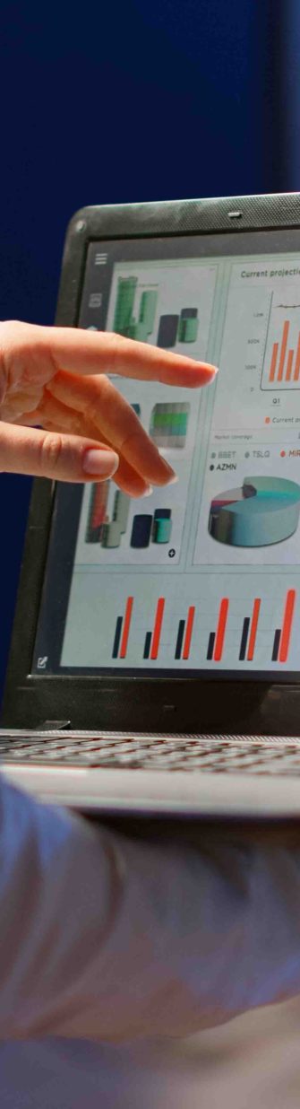 Back view of business woman analysing financial statistics holding laptop standing in start-up office late at night overworking. Busy focused employee using modern technology network wireless overtime